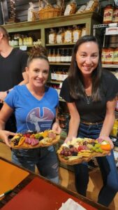 two women posing for a picture with their charcuterie board
